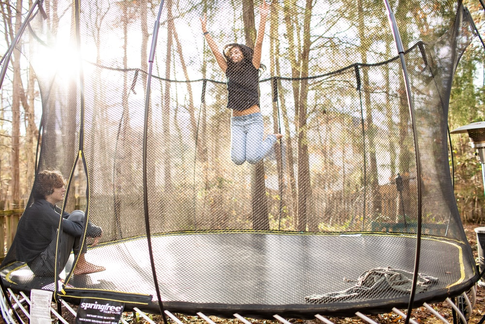 A Girl Mid-Jump on a Trampoline While a Boy Watches from the Sidelines