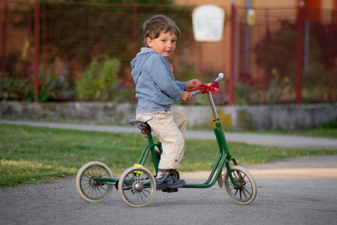 A young boy riding a green tricycle 